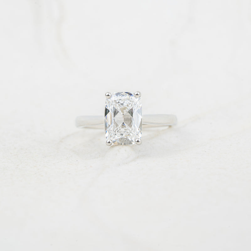 An elongated cushion diamond solitaire ring in a platinum band, set against a light, textured white background.