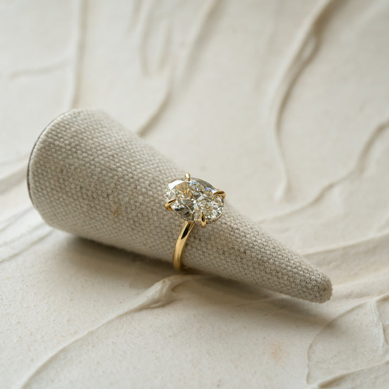 Gold ring with a large 4ct oval cut diamond with hidden halo made in cornwall on a textured beige surface