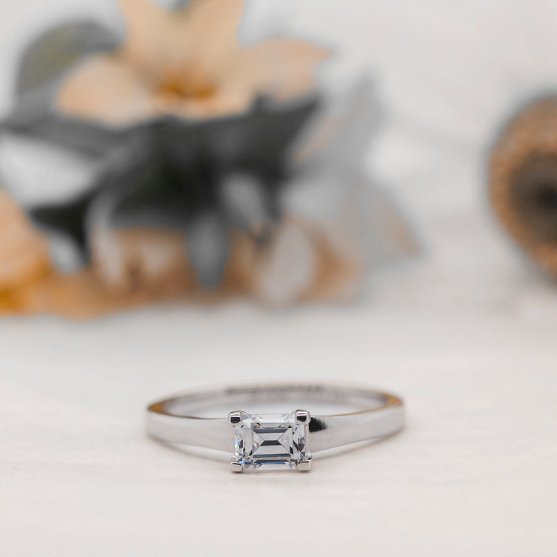 Silver ring with a diamond on a light background with floral accents in background