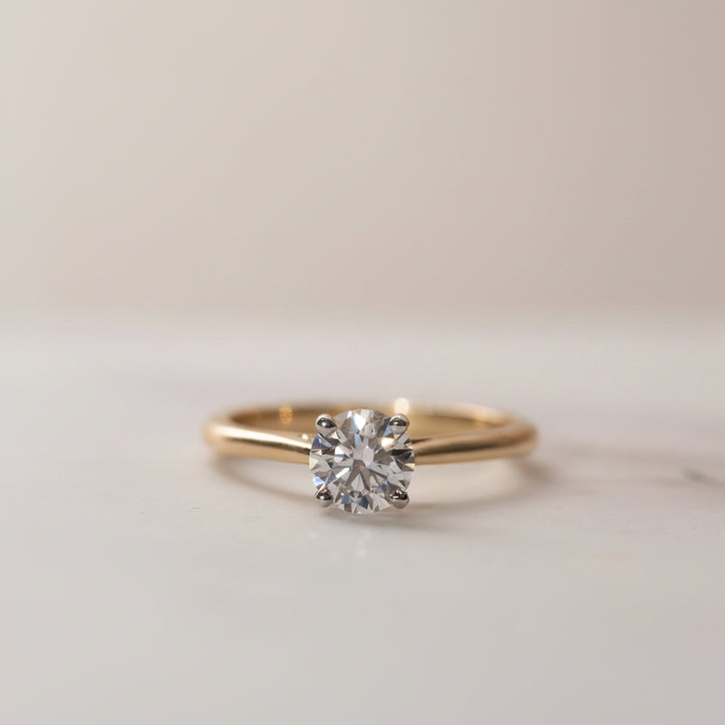 A round lab diamond classic solitaire engagement ring with a gold band, displayed against a floral background.