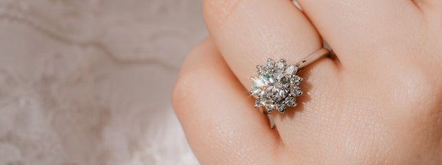 Halo lab-grown diamond engagement ring worn on models hand, sparkling in sunlight with the models lacy white blouse in background.