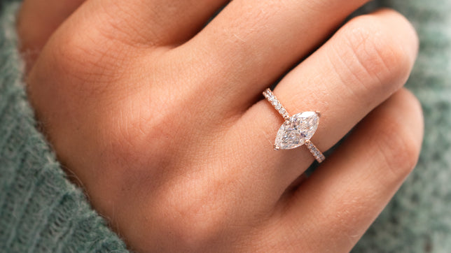 Close up of marquise cut moissanite shoulder set ring worn on models hand with models green jumper in background. 