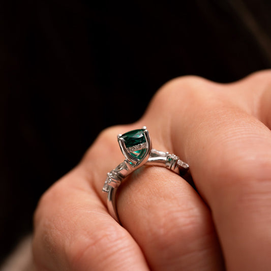 Close up of a hand wearing a white gold hidden halo ring with a emerald gemstone on a dark background by Ethica Diamonds