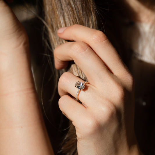 Close-up of a hand wearing a diamond ring while holding hair with a blurred background in direct sunlight