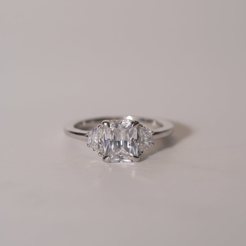 An engagement ring featuring an emerald cut lab diamond centerpiece with half moon cut side stones set in a platinum band.