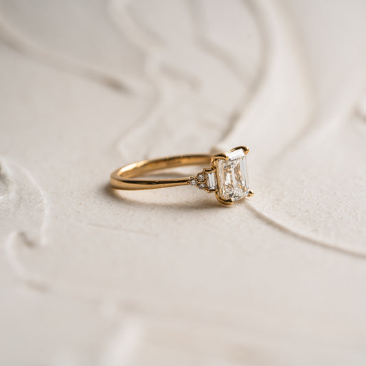 Flat lay of emerald cut man made sustainable diamond ring with baguette and round cut side stones