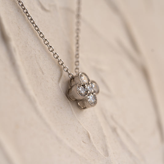 Gold necklace with a leaf shaped diamond pendant on a beige fabric background