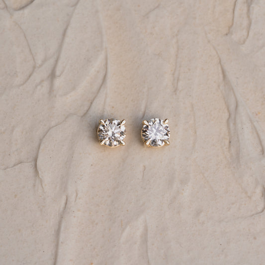 Pair of diamond stud earrings on beige sand