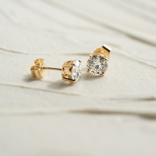 Gold stud earrings with clear gemstones on a light fabric background