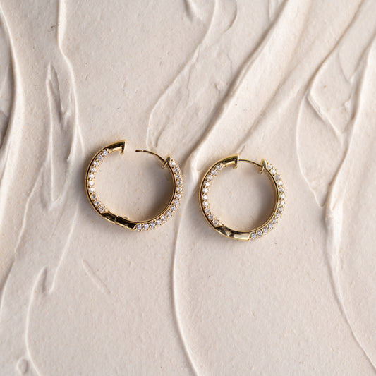 Gold earrings with embedded stones on a textured beige surface