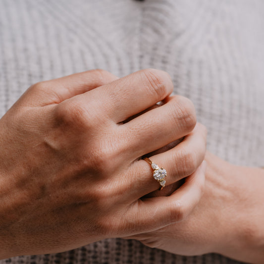 Model wearing rose gold oval pear trilogy engagement ring with knitted blue jumper clasped hands