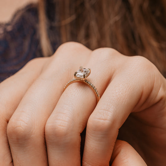 Close-up of a hand wearing a rose gold radiant cut engagement ring with side stones on a blurred background