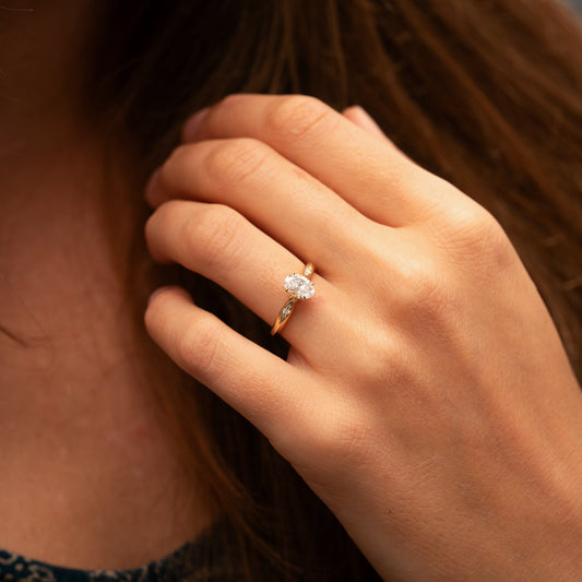 Close-up of a woman wearing an oval cut diamond ring with a knife edge modern detailing to band