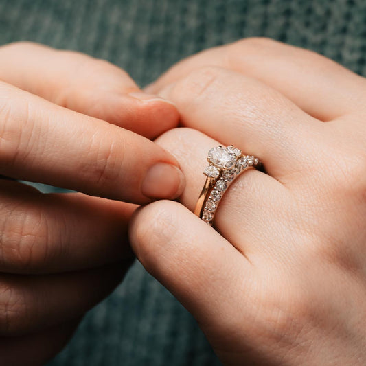 Close up of a hand wearing sustainable oval diamond ring with another hand touching it.