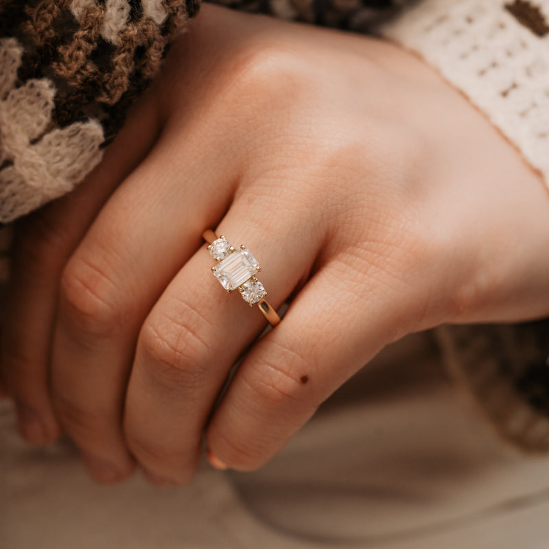 Close-up of The Maya Ring: dainty emerald cut diamond ring with brilliant cut side stones. Trilogy engagement ring design