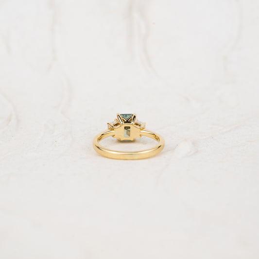Gold ring with a green lab created emerald cut diamond ring on stand with trapezoid sides