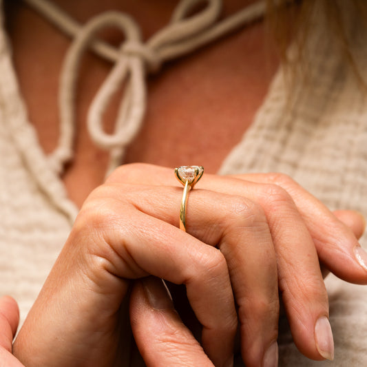 Close-up of a hand wearing a recycled 18k gold ring with a lab created diamond, held by another hand.