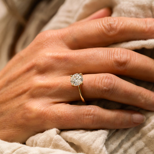 Close-up of a hand wearing a diamond ring on a textured fabric background