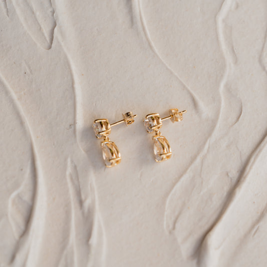 Side view of Harper pear diamond earrings in 9k gold earrings on a textured beige surface