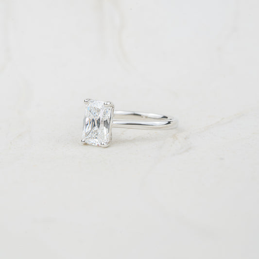 A diamond engagement ring featuring a elongated cushion diamond, photographed on a light marble surface.