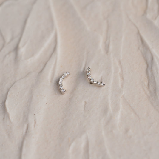 Pair of white gold diamond earrings on a textured beige surface