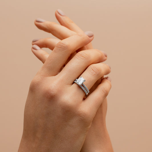 Hands clasping eachother while wearing 2  diamond rings on a beige background