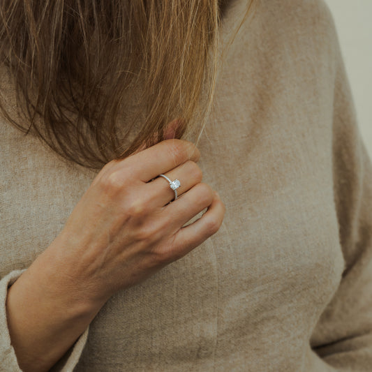 Close-up of a hand wearing a whisper thin hidden halo engagement ring with a neutral background