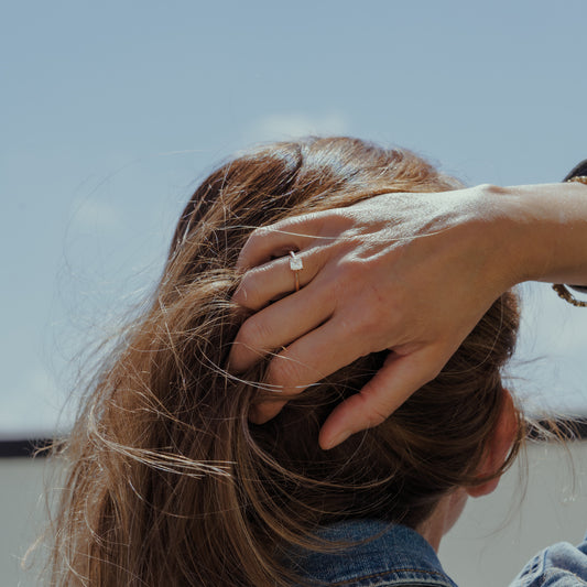 Person with hand in hair against a clear sky wearing a sustainable lab grown diamond ring by ethica diamonds
