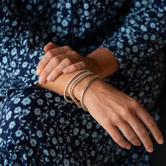Close-up of hands with stacked diamond bracelets on a dark floral-patterned fabric background