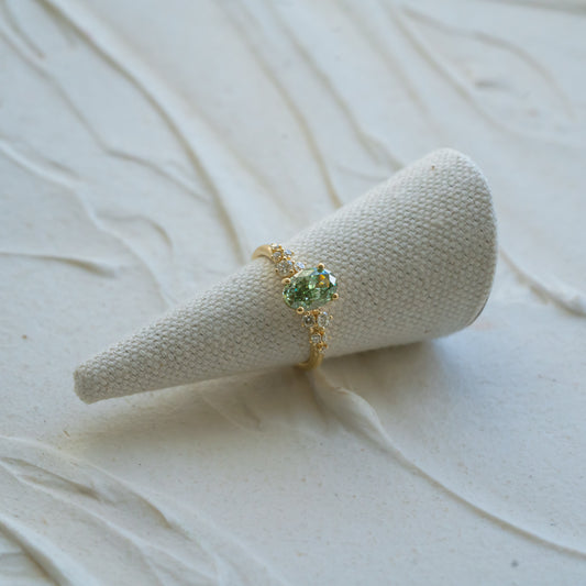 Gold ring with a green gemstone on a textured beige stand against a light background