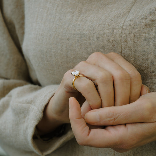 Hand wearing cornish luxury diamond ring with a blurred fabric background made from recycled gold
