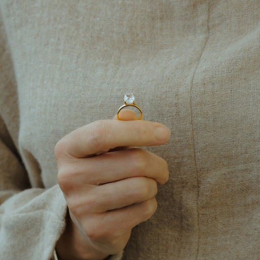 Gold ring with a diamond held between fingers against a beige fabric background