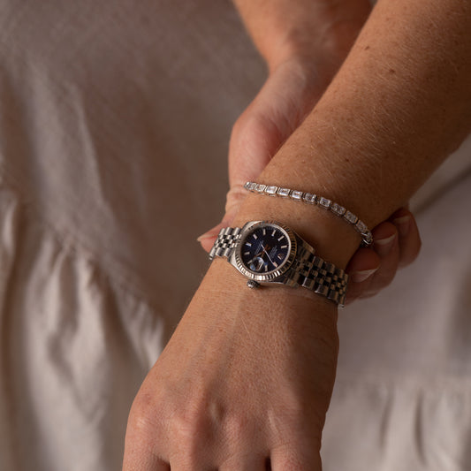 Close-up of a wrist wearing a silver watch stacked with a diamond bracelet 