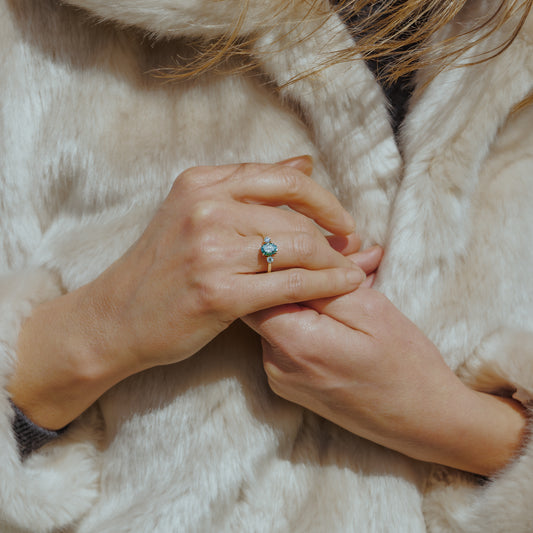 Lady wearing green coloured diamond ring in yellow gold with light fur coat