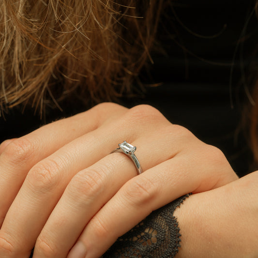 Close-up of a hand wearing a diamond ring with a blurred background wearing satin black lace dress and modern minimalist diamond ring
