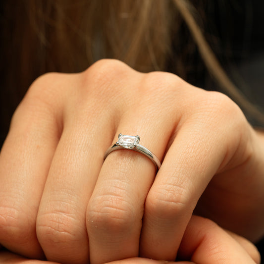 Close-up of a hand wearing a diamond ring with a blurred background. Rectangular diamond antique inspired emerald cut and rounded tapered shank