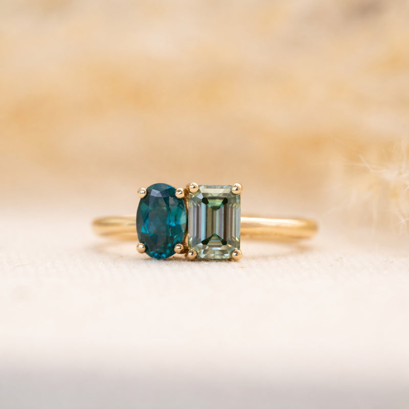 Gold ring with two green lab created gemstones paraiba spinel and moissanite on a gradient background