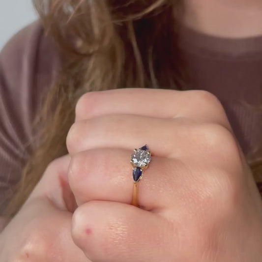Model wears round engagement ring with pear side stones sapphire blue accents in yellow