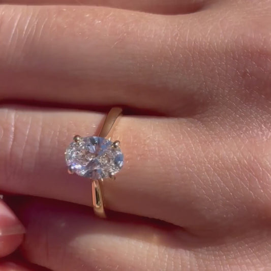 Model shows yellow 18k gold soliaire engagement ring with 1.5 carat oval cut lab grown diamond
