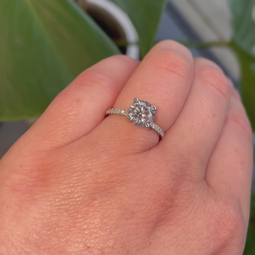 Slim band shoulder set engagement ring with round cut diamond set into 4 claws shot on hand