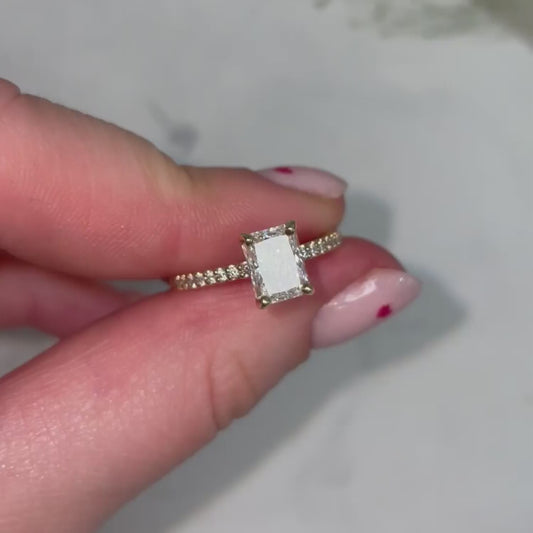 model holds dainty elegant emerald radiant cut engagement ring with diamond pave shoulder set melee and modern look