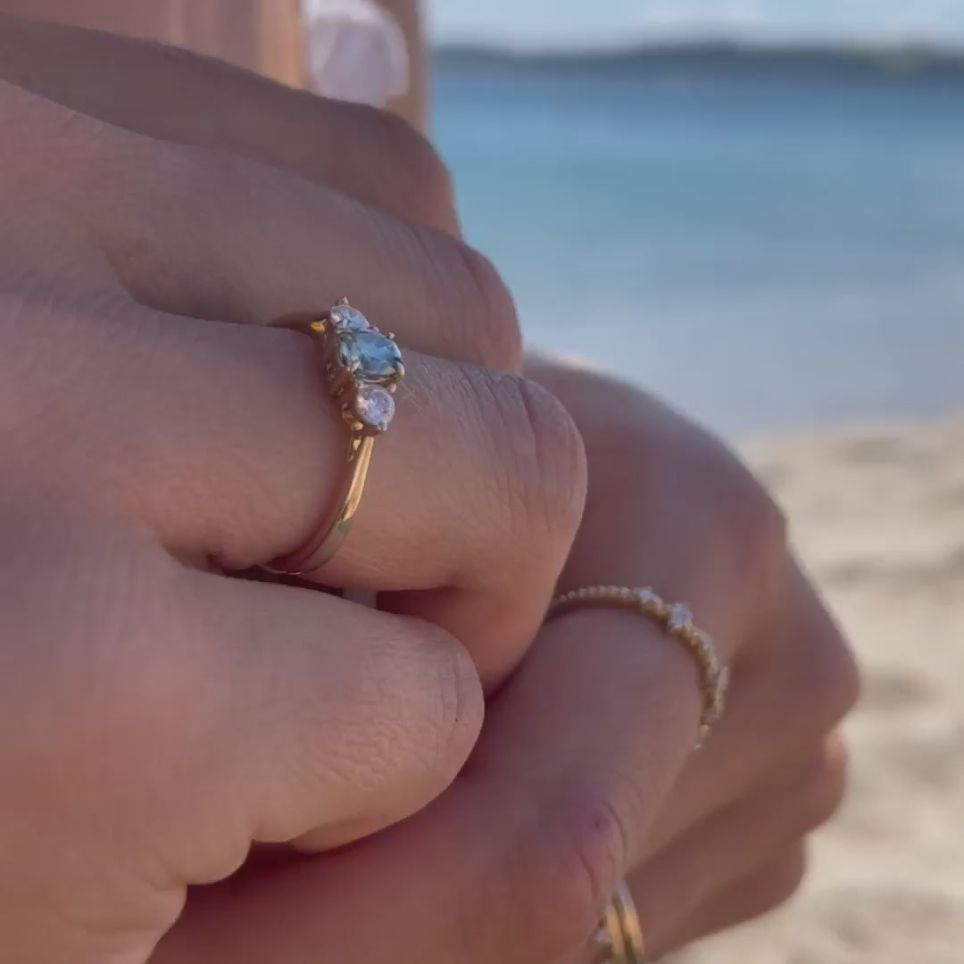 Model wearing dark green moissanite ring on cornish beach next to blue water